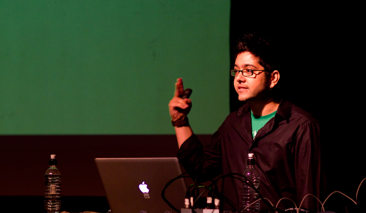 Me on stage at Flash on the Beach, presenter remote in hand, a MacBook and a green slide behind